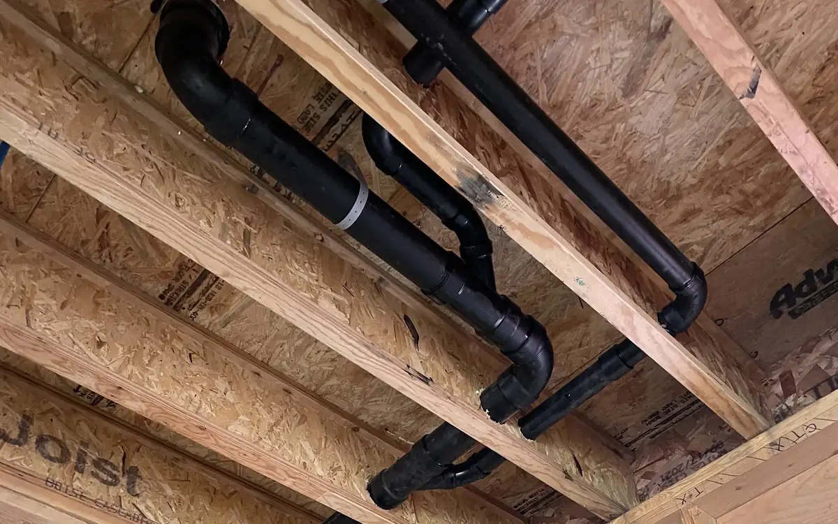 Black ABS drain and vent lines run through the floor joists of a new build, plumbed by All Valley